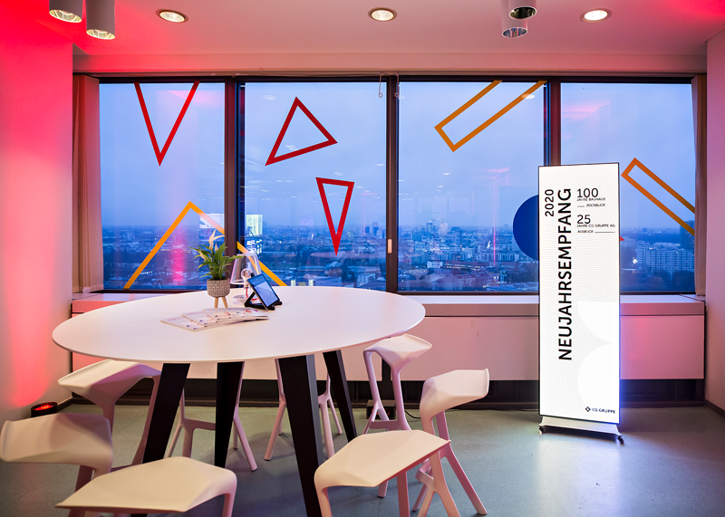 Digitales Roll-Up beim Neujahrsempfang in einem modernen Raum mit Panoramafenstern und Stehtisch.